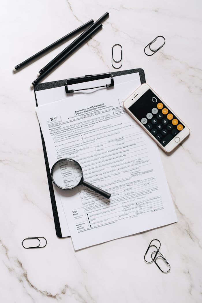 High angle shot of tax form, magnifying glass, and smartphone calculator on marble surface.